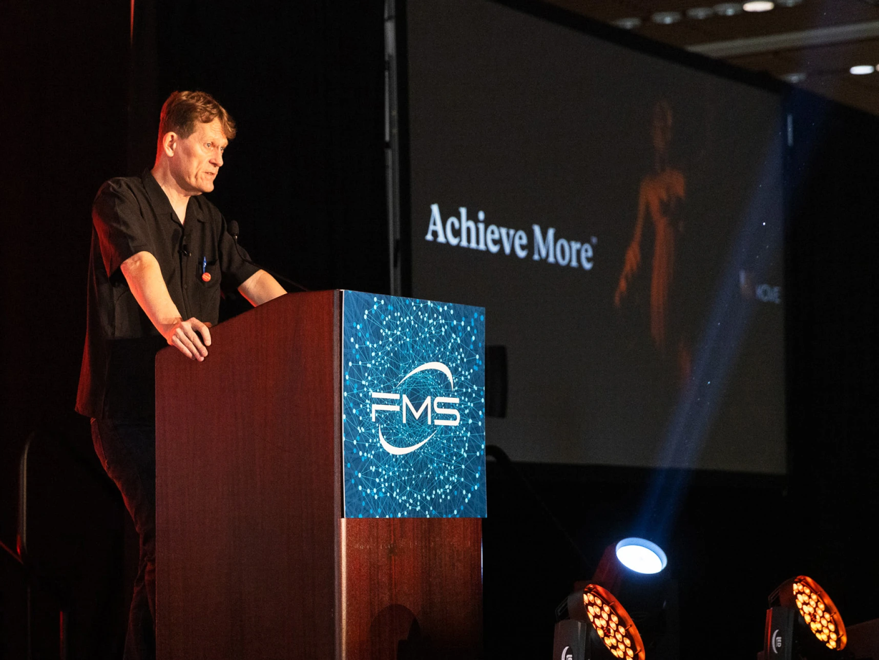 Speaker at FMS event, "Achieve More" on screen.