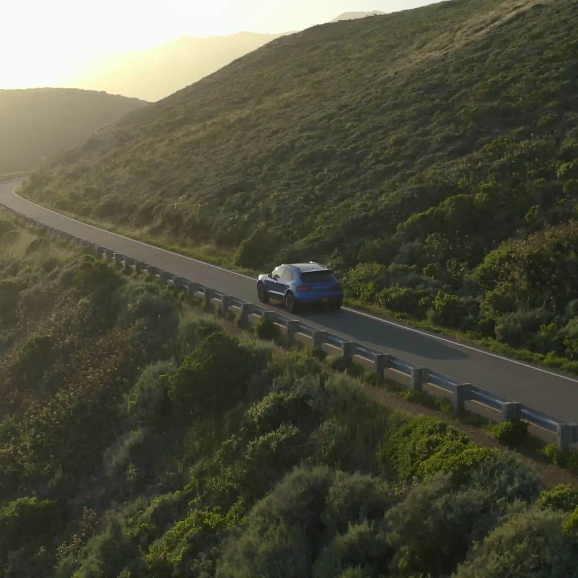 Blue car driving on a scenic coastal highway with green hills.