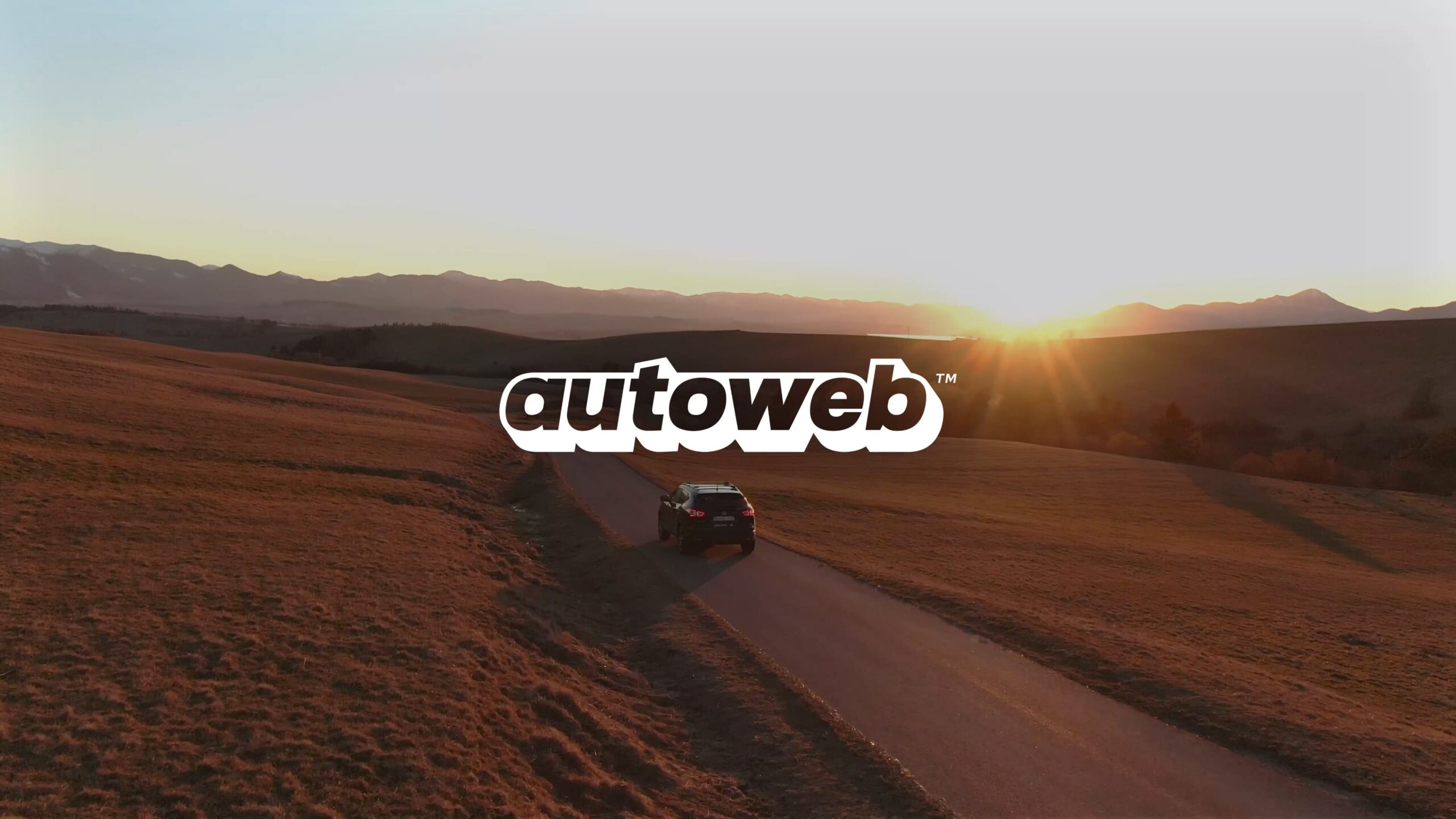 Autoweb: Car driving on a winding road at sunset with mountains in the background.