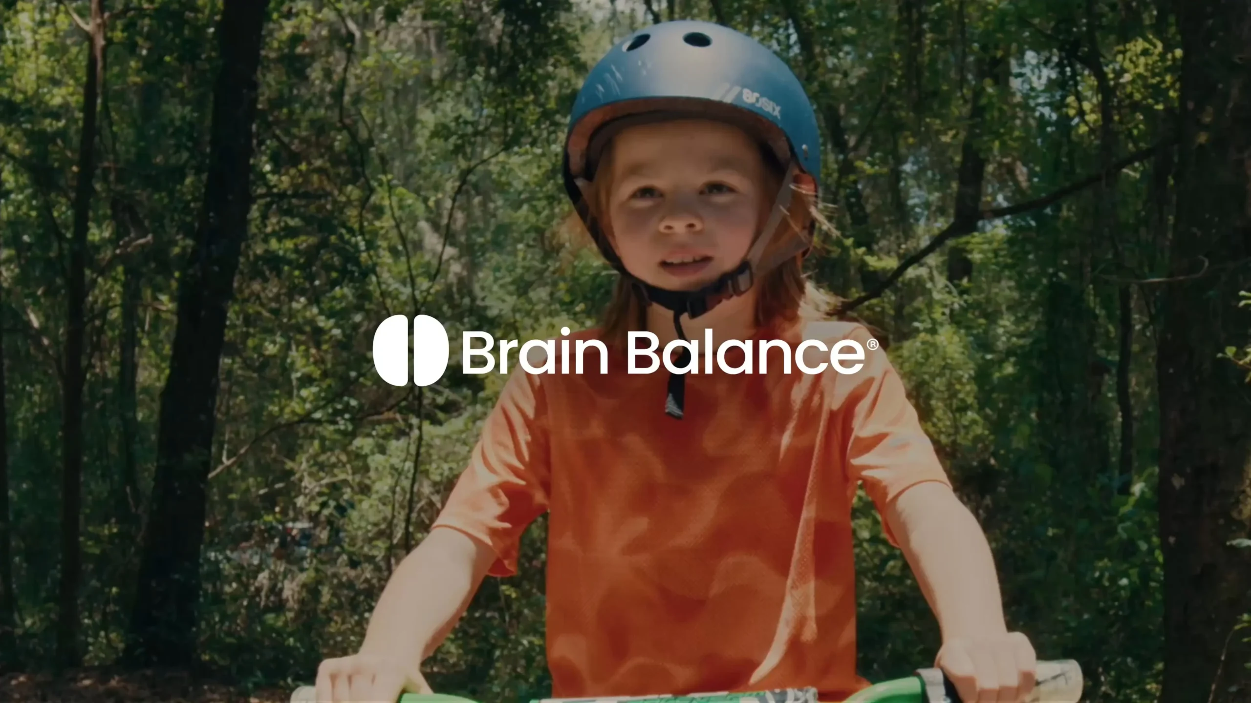 Child wearing a helmet riding a bike in the woods. Brain Balance.